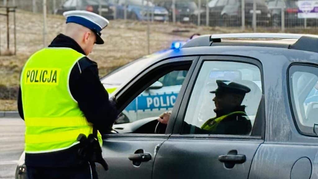 Policjant przeprowadza kontrolę na drodze, stojąc obok zatrzymanego samochodu.