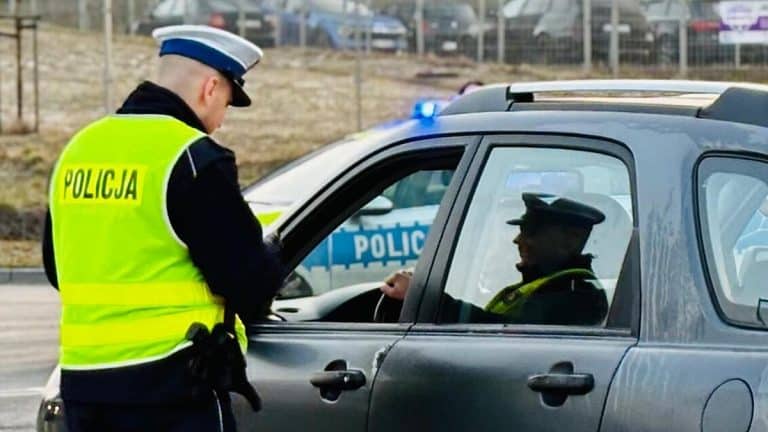 Policjant przeprowadza kontrolę na drodze, stojąc obok zatrzymanego samochodu.
