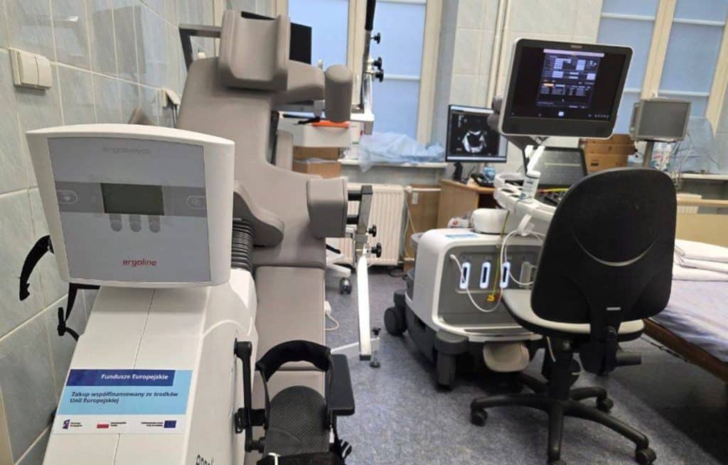 Nowoczesny sprzęt diagnostyczny w olsztyńskim szpitalu, w tle komputery i ł&oacute;żko pacjenta.