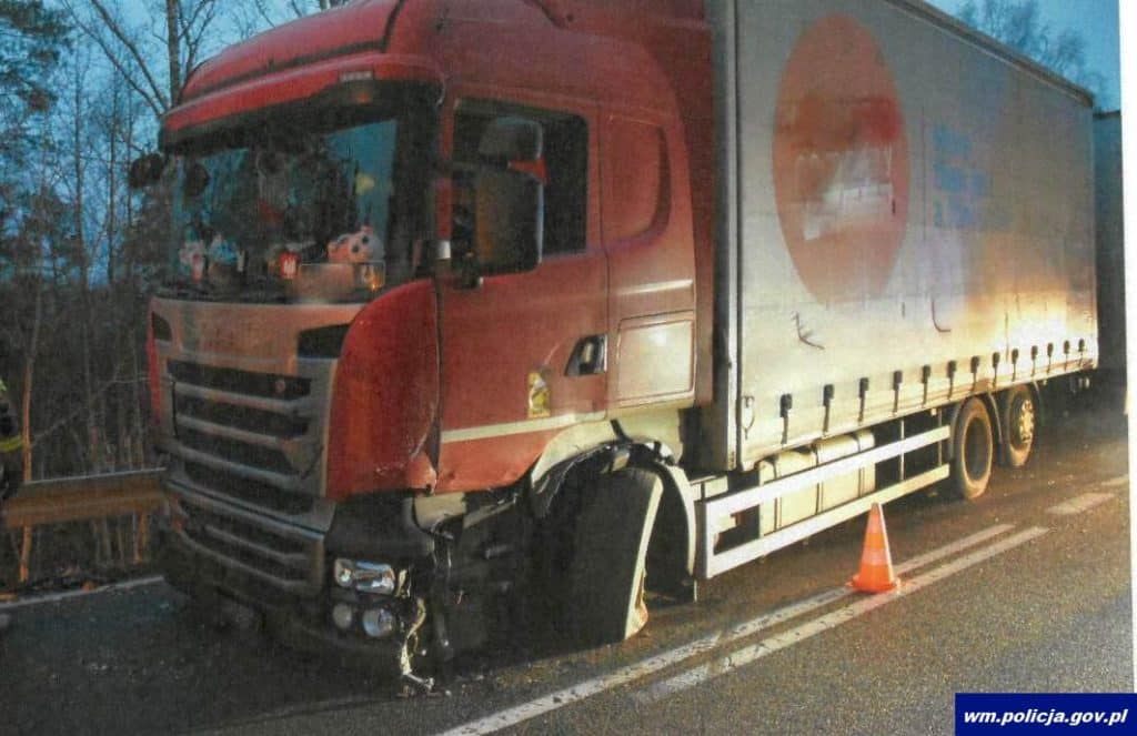 Uszkodzony samoch&oacute;d ciężarowy na drodze krajowej po wypadku, na miejscu stała odblaskowa taśma ostrzegawcza.