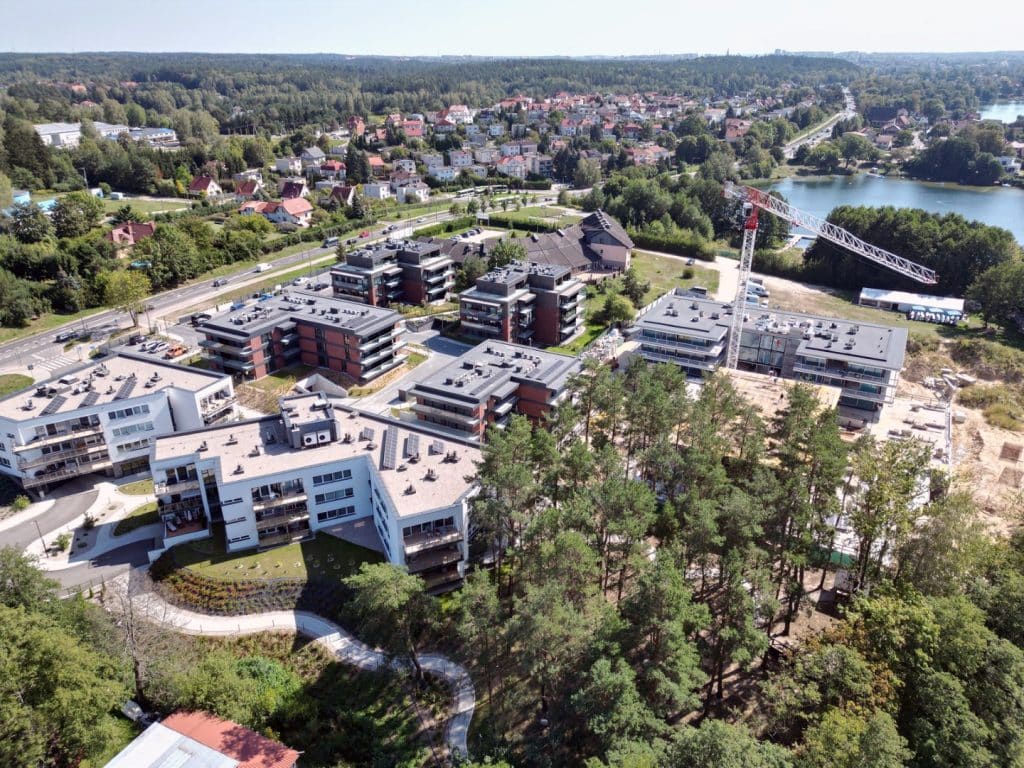 Widok na rozwijające się osiedle mieszkaniowe w pobliżu jeziora Ukiel, otoczone lasami i terenami rekreacyjnymi.