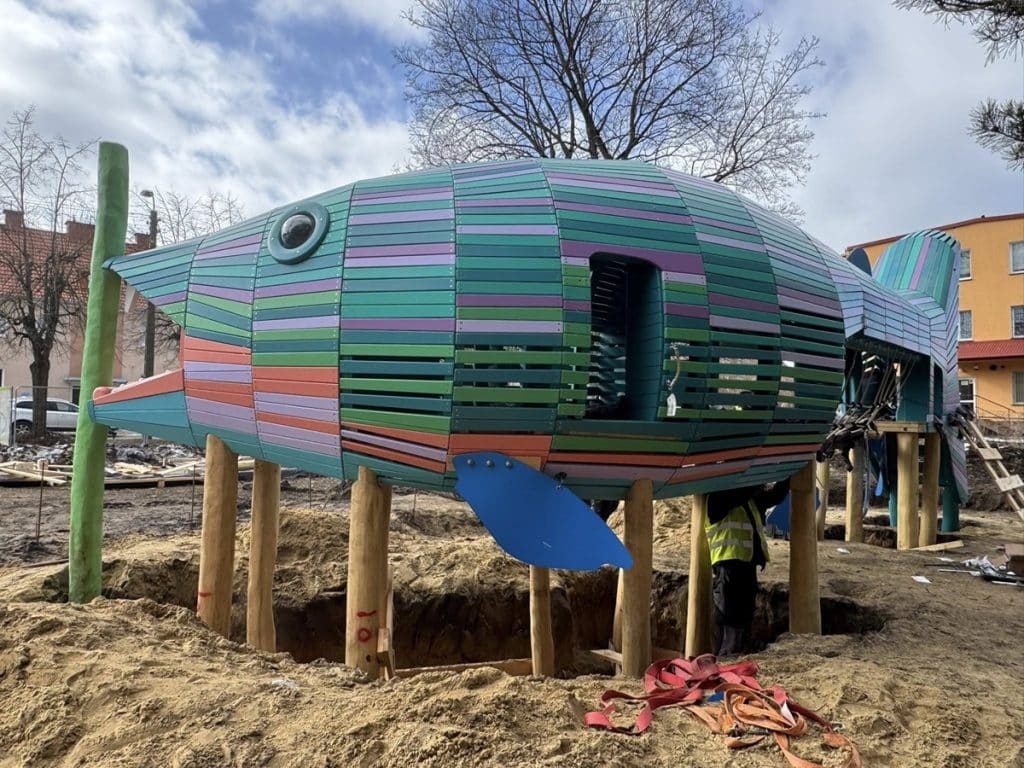 Kolorowa konstrukcja przypominająca rybę na placu budowy w Giżycku, w trakcie montażu.