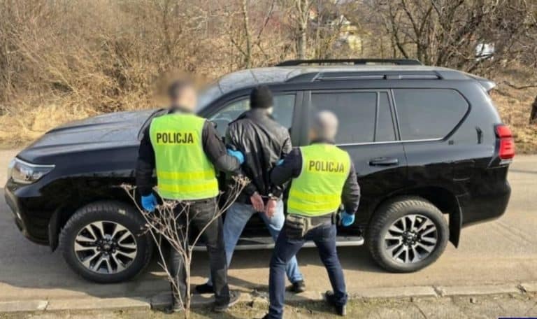 Policjant po służbie zatrzymuje podejrzanego na ogr&oacute;dkach działkowych, trzymając go za ręce.