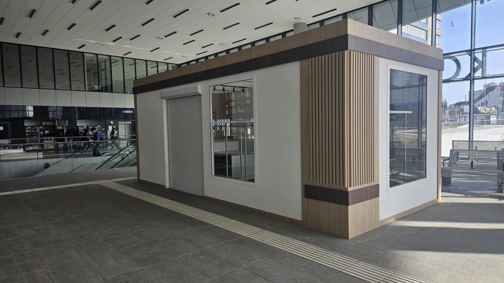 Nowa wyspa handlowa w holu dworca Olsztyn Gł&oacute;wny, wykonana z drewna i szkła, w centrum uwagi pasażer&oacute;w.