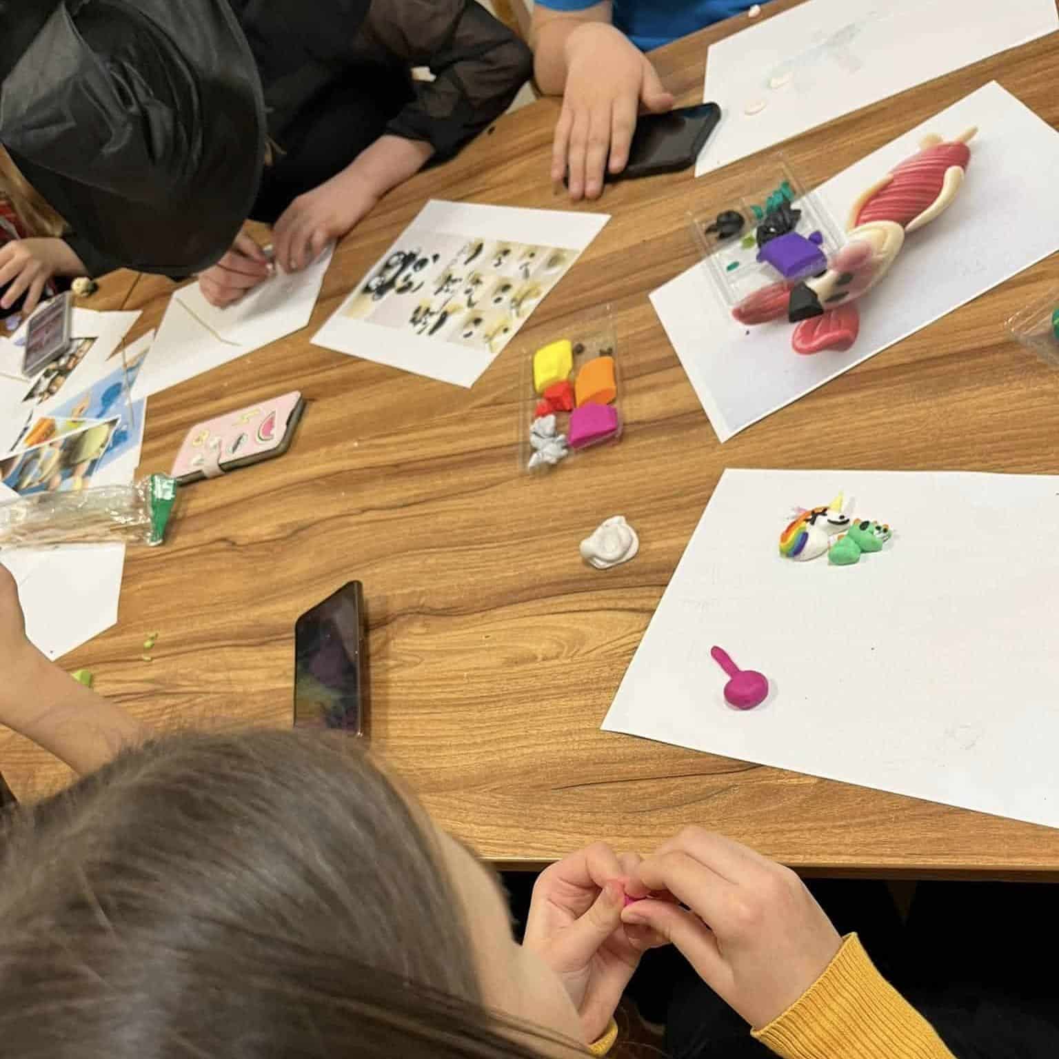 Dzieci podczas zajęć artystycznych, tworzące z modeliny i korzystające z r&oacute;żnych materiał&oacute;w.