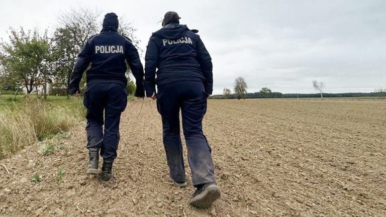 Policjanci szukają zaginionego mężczyzny na polu, odzież w policyjnych kurtkach, jesienna pogoda.