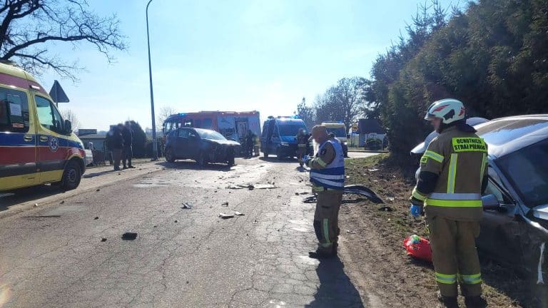 Widok na miejsce poważnego zderzenia dw&oacute;ch samochod&oacute;w osobowych z załogą ratunkową i śmigłowcem LPR na drodze.