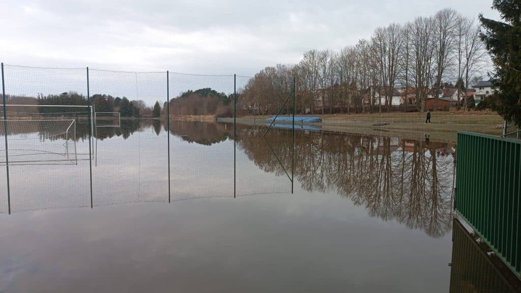 Zalane boisko sportowe we Fromborku, woda sięga do poziomu ogrodzenia.