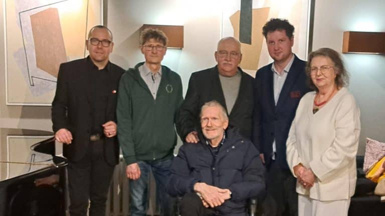 Grupa os&oacute;b na spotkaniu, w tym mężczyzna na w&oacute;zku inwalidzkim, w pomieszczeniu z mapami na ścianach.