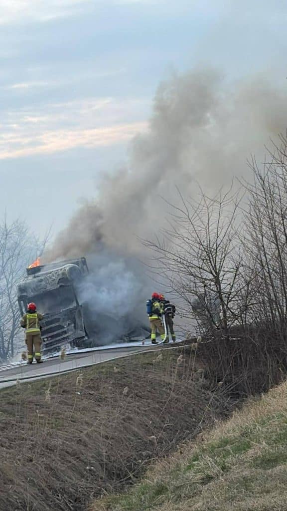 Pożar ciężar&oacute;wki na drodze w Elblągu, widoczne płomienie i dym, strażacy gaszą pojazd.