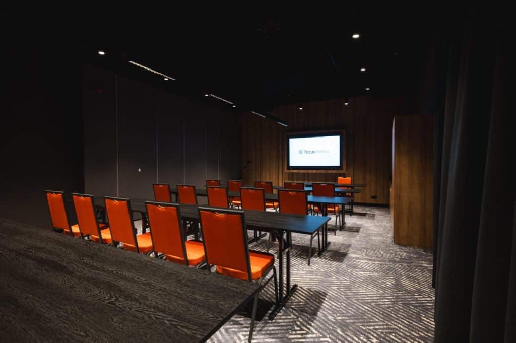 Wnętrze nowoczesnego hotelu z salą konferencyjną, czarne ściany i pomarańczowe krzesła.