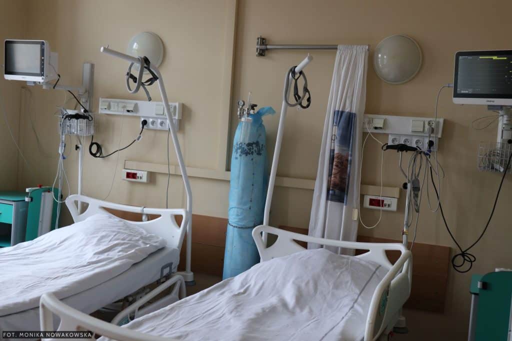 Puste ł&oacute;żka w szpitalnej sali z urządzeniami medycznymi i sprzętem.