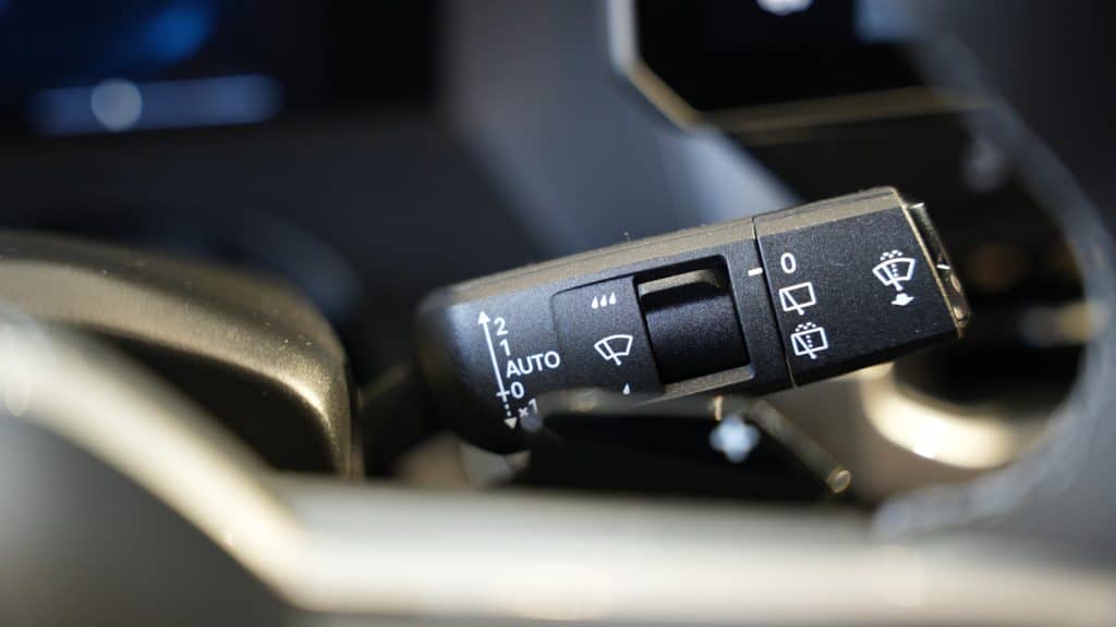 Przedni panel wycieraczek samochodu z symbolami i regulacją, widoczny w zbliżeniu.