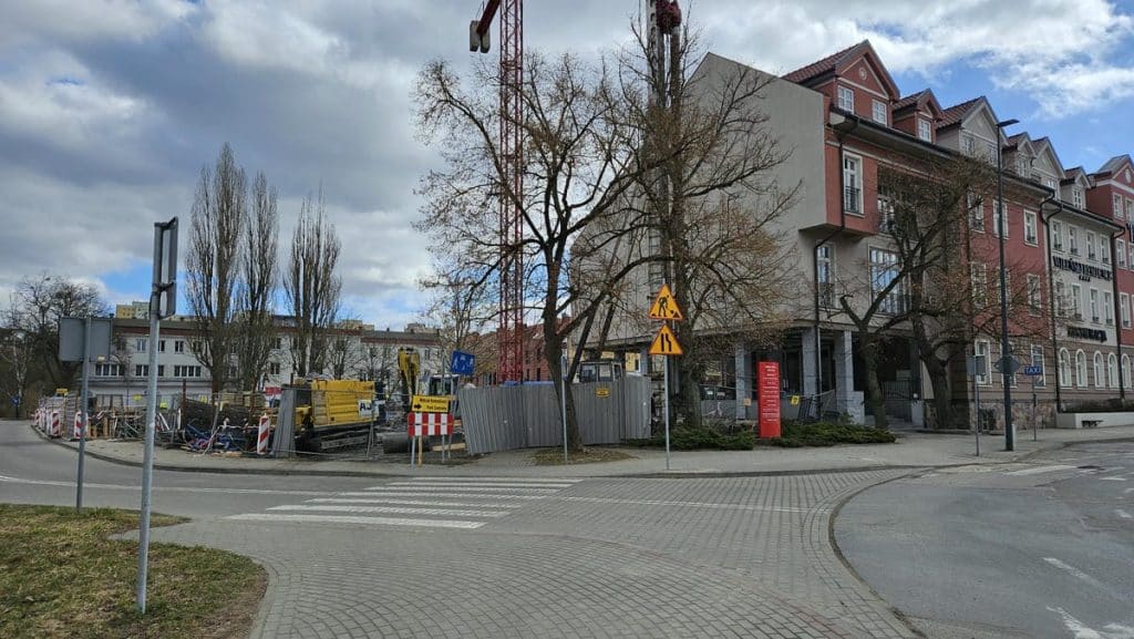 Trwa budowa nowego obiektu usługowego w centrum Olsztyna, widoczne prace ziemne i rusztowania.