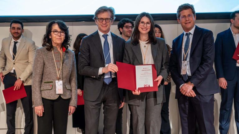 Grupa ludzi na konferencji, jedna osoba otrzymuje certyfikat, w tle ekran projekcyjny.