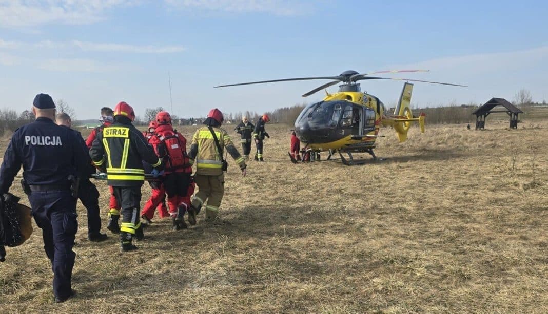 Służby ratunkowe na polu przy jeziorze Linowo, helikopter w tle, akcja ratunkowa na miejscu.