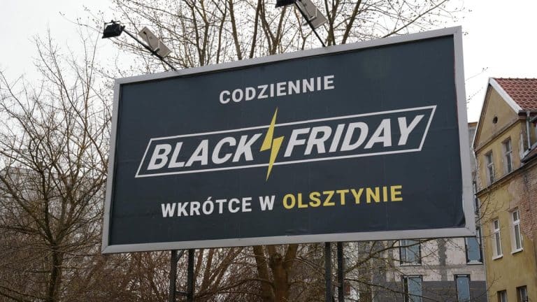 Billboard w Olsztynie z napisem 'Codziennie Black Friday' i 'Wkr&oacute;tce w Olsztynie', na tle drzew i budynk&oacute;w.