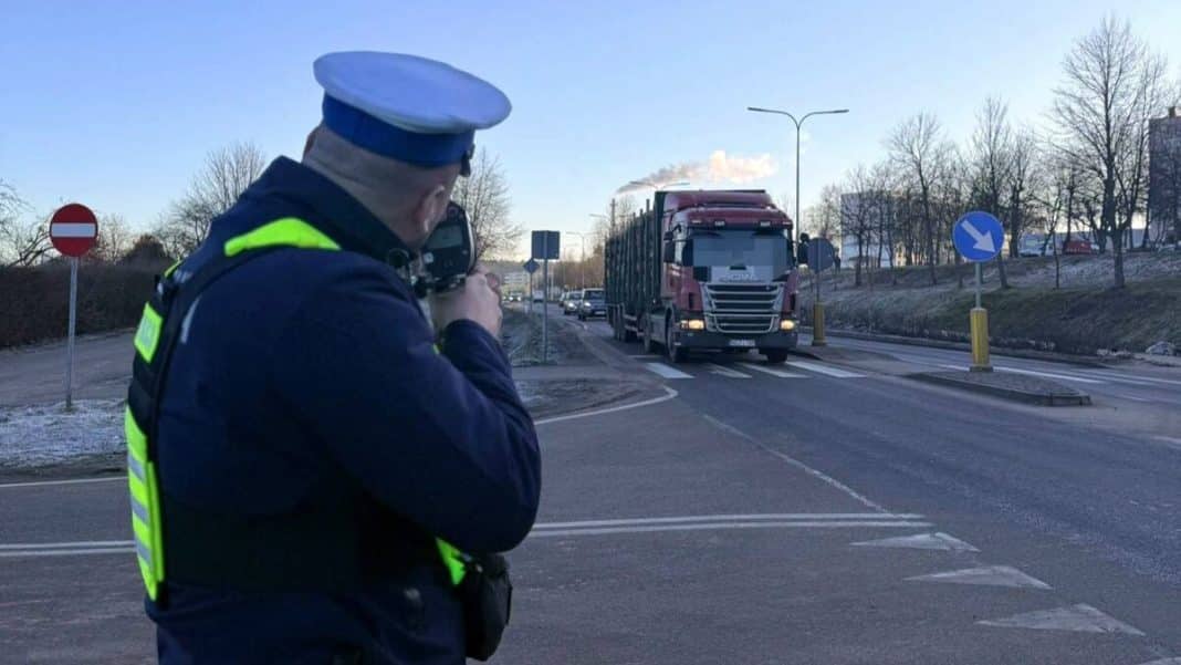 Policjant robi zdjęcie na drodze, w tle samochody i znaki drogowe.