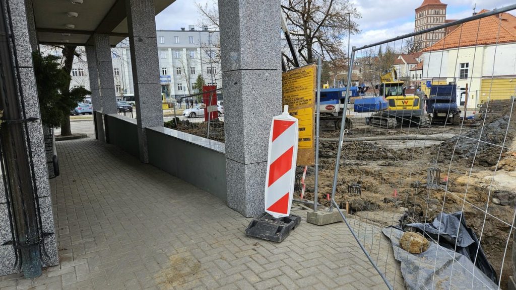 Trwa budowa nowego obiektu usługowego w centrum Olsztyna, widoczne wykopy i prace konstrukcyjne.