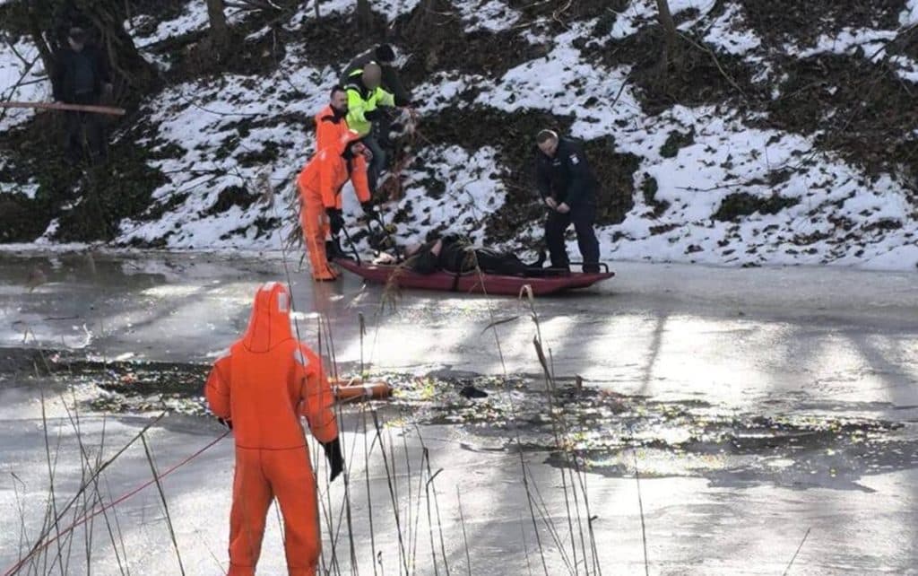 Ratownicy i policjanci pomagają mężczyźnie wyciągniętemu z zamarzniętej rzeki, akcja ratunkowa na lodzie.