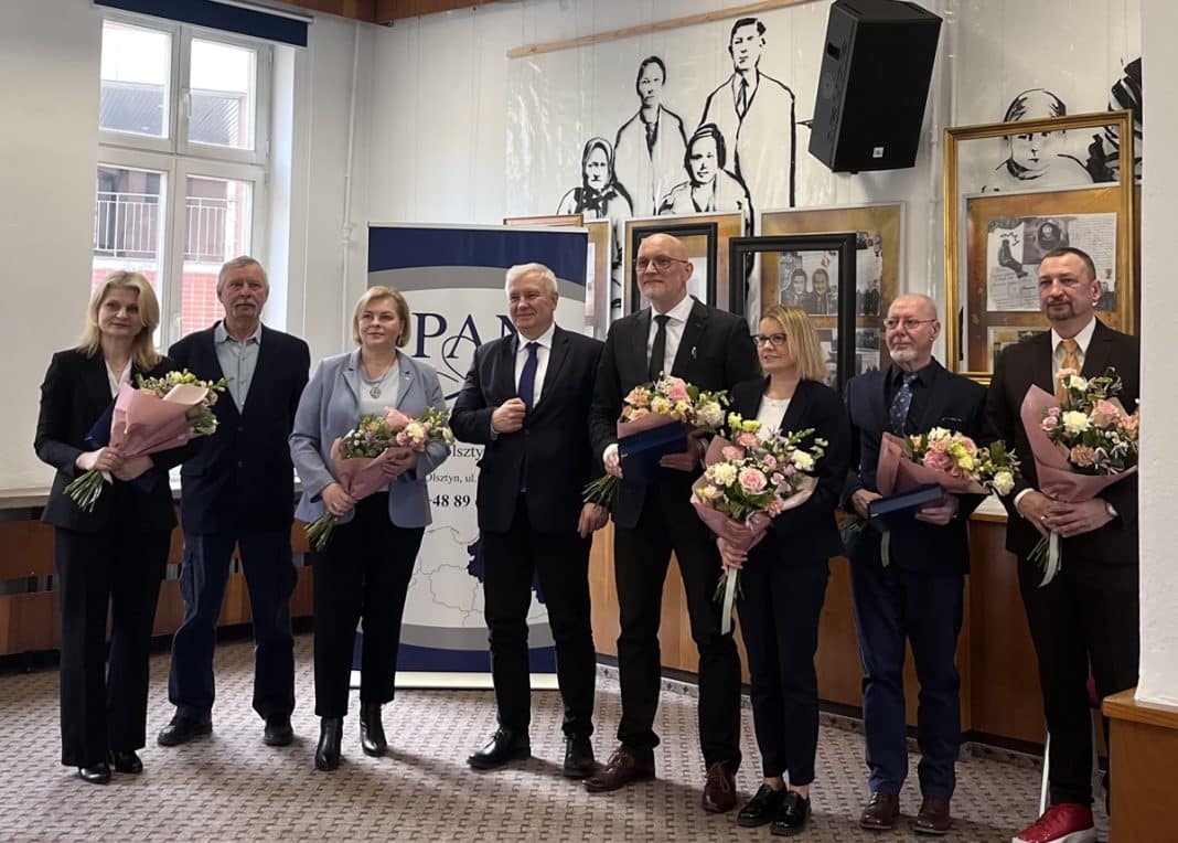 Grupa naukowc&oacute;w z Olsztyna podczas uroczystości wręczenia nagr&oacute;d PAN, trzymający kwiaty i dyplomy.