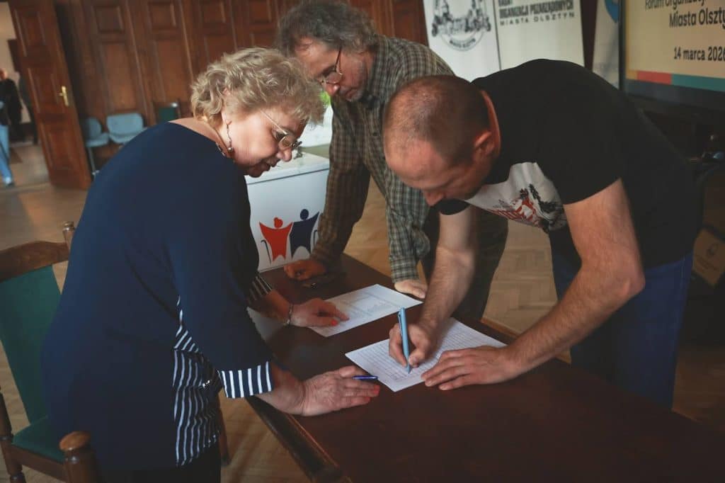 Osoby podpisujące dokument podczas spotkania organizacji społecznych w Olsztynie.