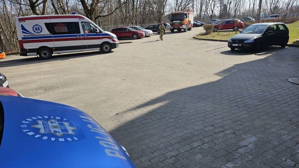 Widok na miejsce zdarzenia z udziałem służb ratunkowych na osiedlu w Olsztynie, w tle budynek i samochody.