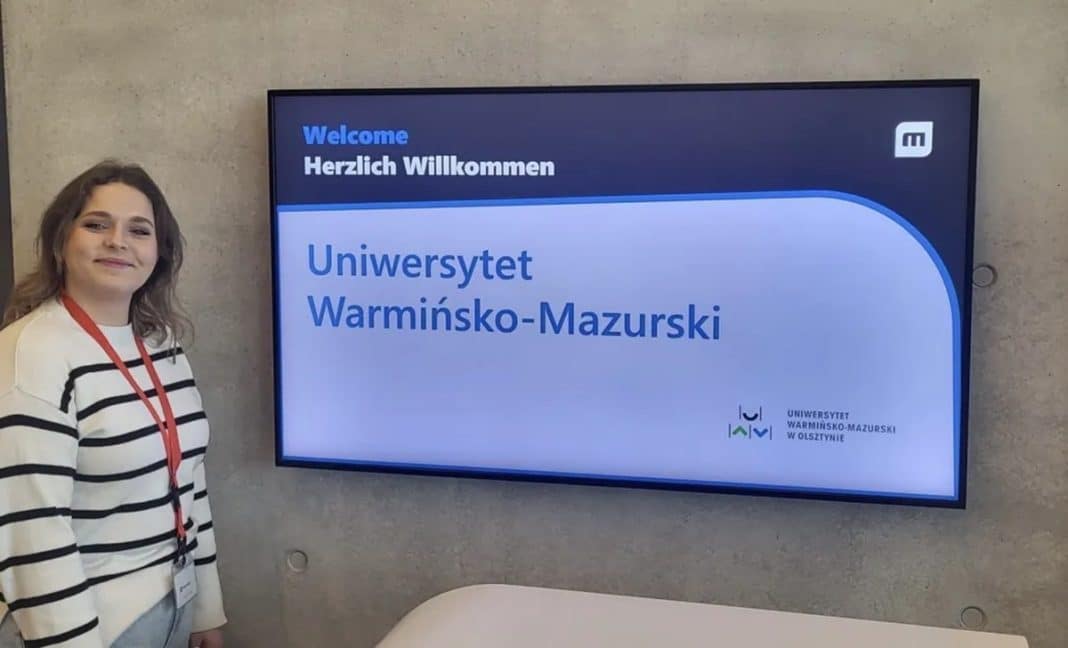 Uczestniczka konkursu przed ekranem z napisem o Uniwersytecie Warmińsko-Mazurskim w Olsztynie.