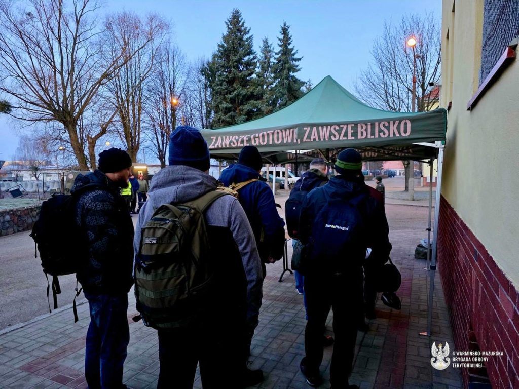 Grupa ochotnik&oacute;w czeka pod namiotem w koszarach w Braniewie, przygotowując się do szkolenia w WOT.