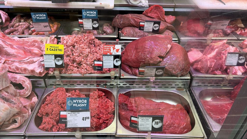 Mięso i wędliny na stoisku w sklepie Intermarch&eacute; Olsztyn, w tym biała kiełbasa i r&oacute;żne rodzaje mięsa.