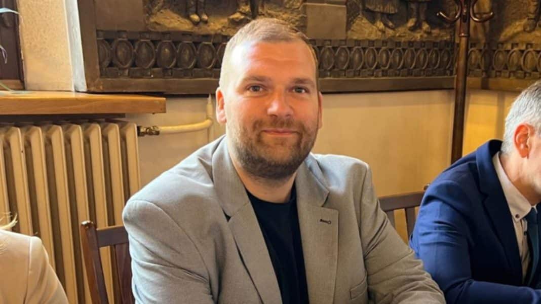 Zdjęcie mężczyzny w jasnym garniturze, siedzącego przy stole podczas spotkania.