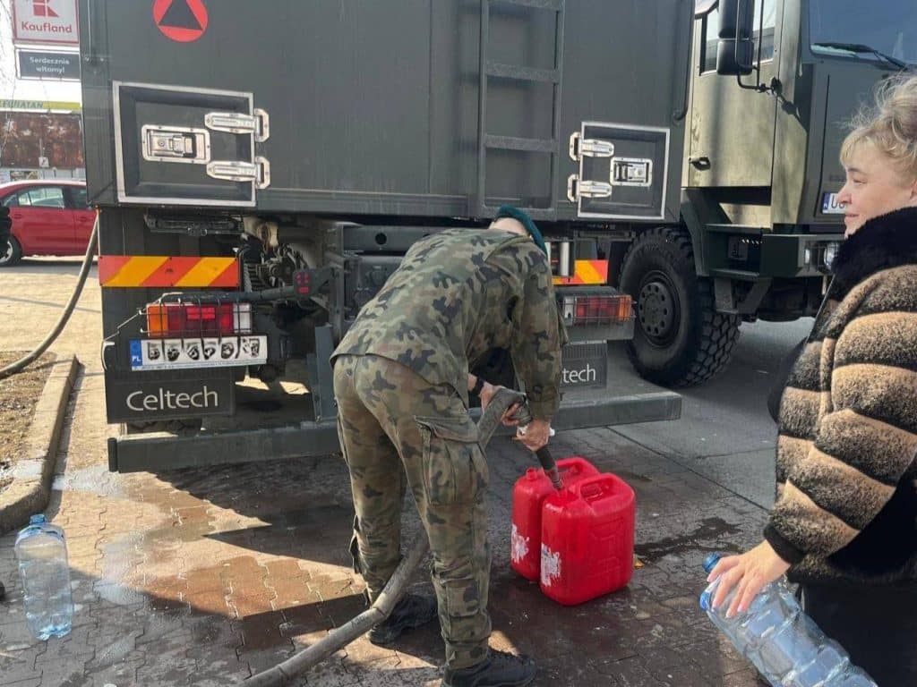 Żołnierz napełnia kanistry wodą z cysterny w mieście, obok kobieta z butelką.