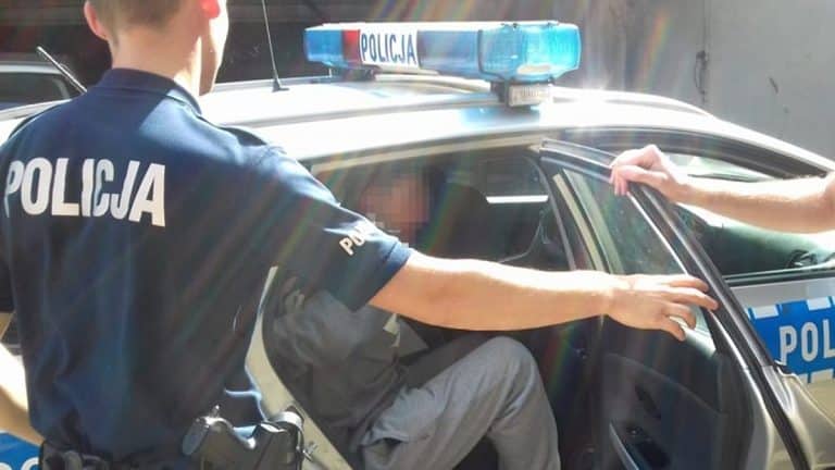 Policjant pomaga osobie siedzącej w radiowozie, w tle służbowe oznaczenia.