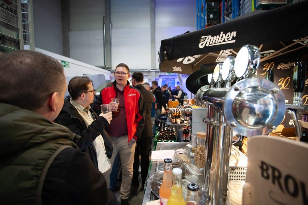 Uczestnicy targ&oacute;w biznesowych w Gdańsku rozmawiają przy stoisku z napojami i produktami spożywczymi.