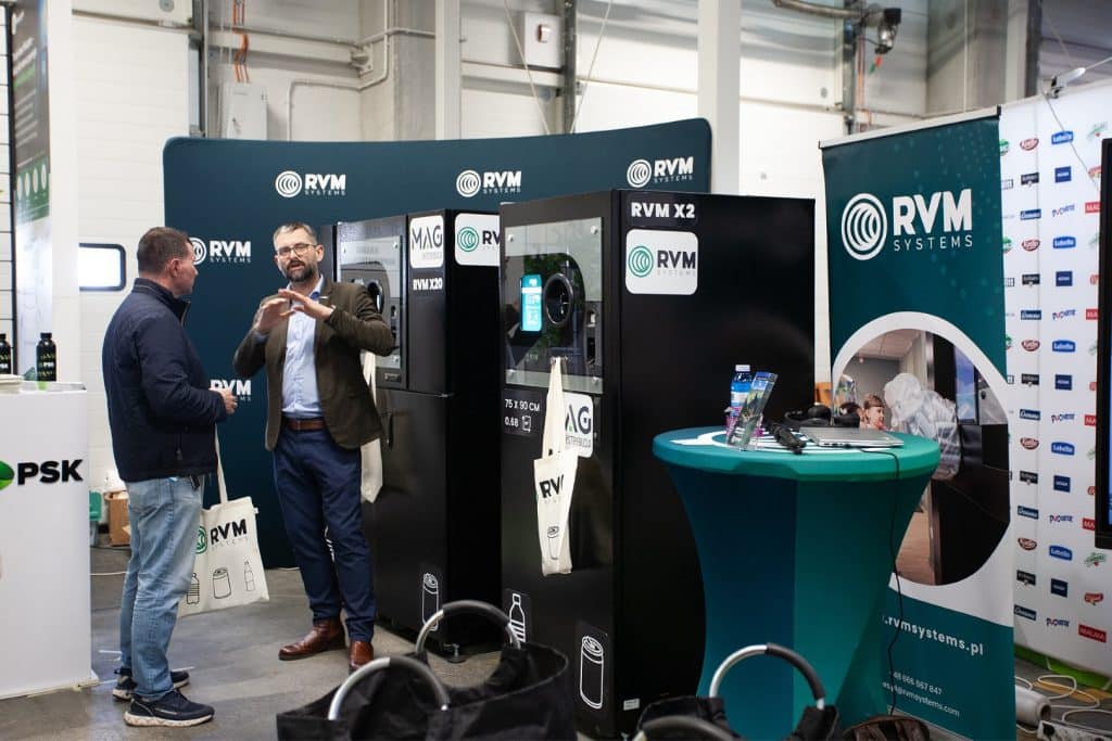Uczestnicy rozmawiają przy stoisku z urządzeniami do automatyzacji w branży HoReCa i handlu.
