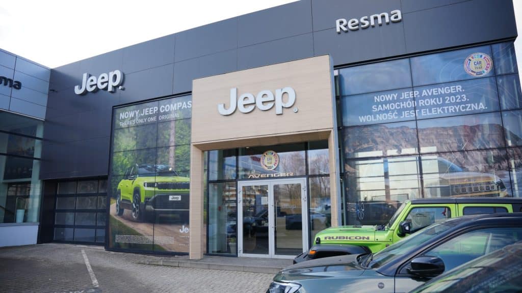 Widok na salon samochodowy Jeep w Olsztynie z dużymi ekranami i samochodami na parkingu przed wejściem.