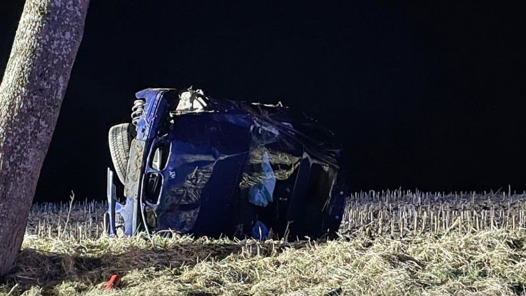 Uszkodzone BMW po wypadku, dachujące na poboczu drogi wojew&oacute;dzkiej, nocą.