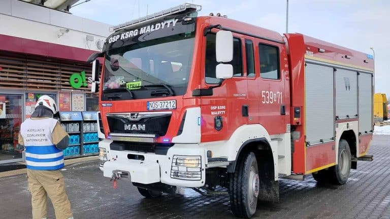 Straż pożarna na stacji paliw Orlen przy S7 po pożarze samochodu, w tle sklep spożywczy.