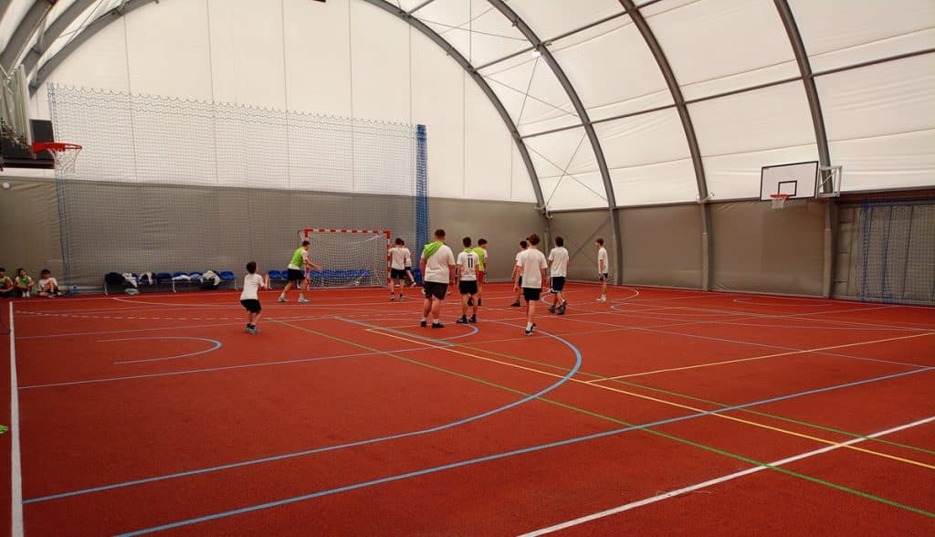 Młodzi sportowcy grają na zadaszonym boisku w hali sportowej.