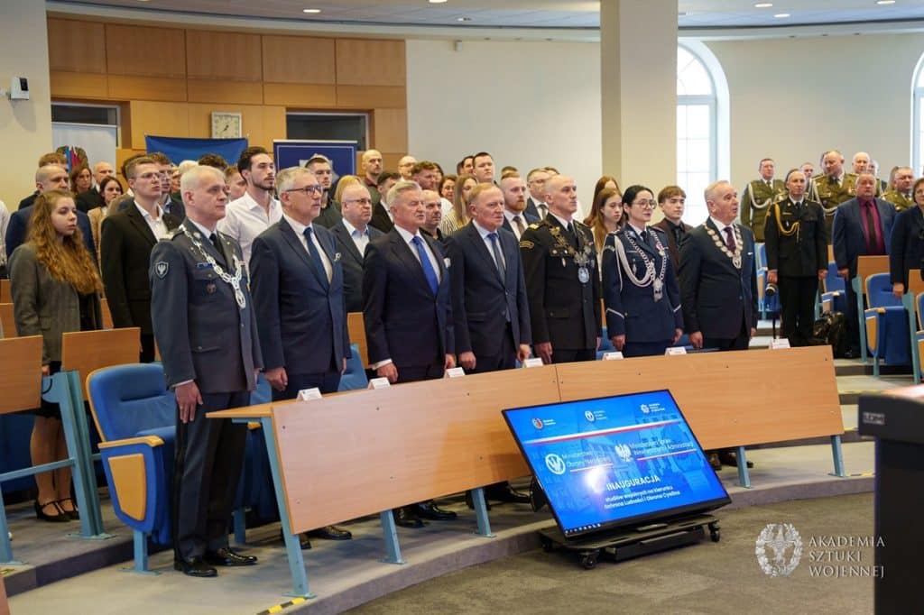 Uczestnicy uroczystości inauguracji nowego kierunku studi&oacute;w w sali konferencyjnej, wśr&oacute;d nich osoby w mundurach i formalnych strojach.