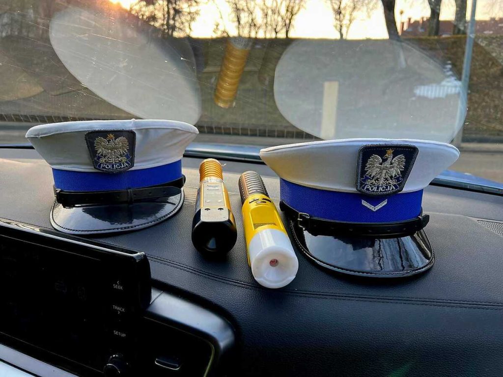 Policja na Warmii i Mazurach przeprowadza kontrole drogowe, na zdjęciu policyjne czapki i urządzenia pomiarowe na desce rozdzielczej samochodu.