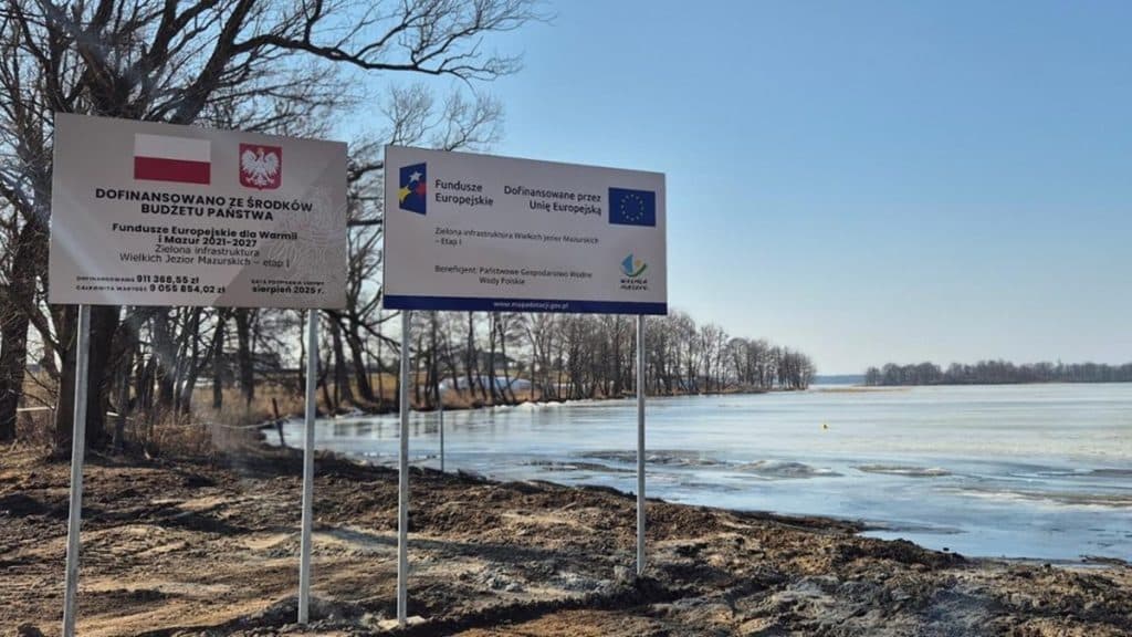 Tablica informacyjna przy zamarzniętym jeziorze na Mazurach, wskazująca na zakończenie modernizacji kanału.