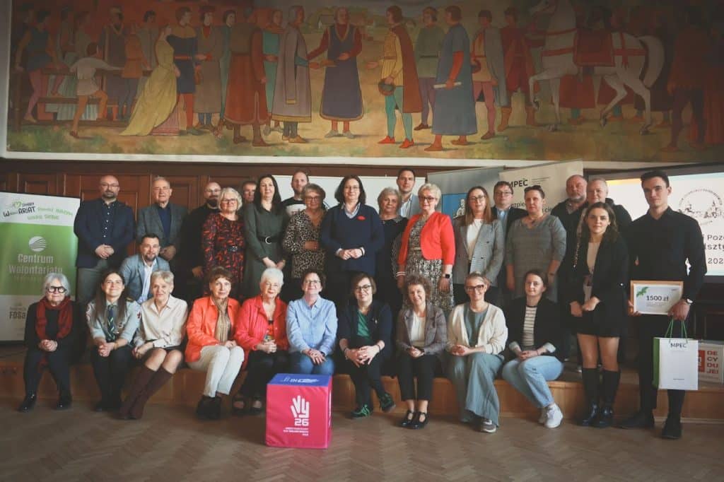 Grupa os&oacute;b na spotkaniu organizacji społecznych w sali konferencyjnej, w tle duży mural.