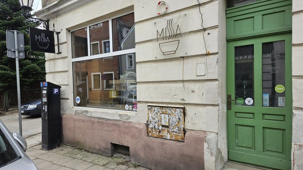 Zamknięte wejście do lokalu na olsztyńskiej Star&oacute;wce, zielone drzwi i puste okno, na ścianie widoczny znak Missa.