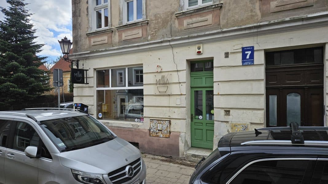 Widok na zamknięty lokal przy ul. Lelewela na olsztyńskiej Star&oacute;wce, z samochodami na pierwszym planie.