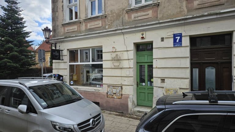 Widok na zamknięty lokal przy ul. Lelewela na olsztyńskiej Star&oacute;wce, z samochodami na pierwszym planie.