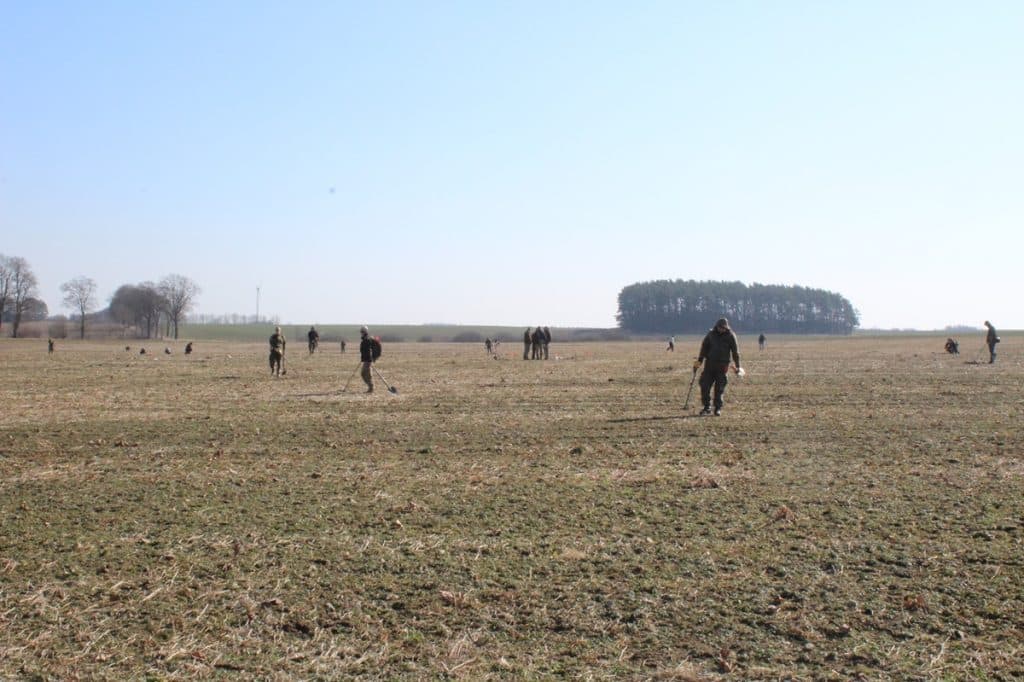 Grupa archeolog&oacute;w poszukuje artefakt&oacute;w na polu w okolicach wsi Leszcz, w tle niewielki lasek i szeroka r&oacute;wnina.