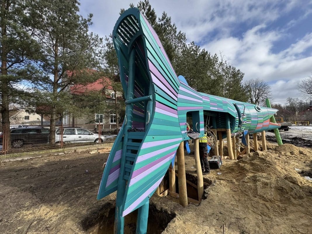 Budowa dużej, kolorowej konstrukcji w kształcie ryby na zielonym skwerze w Giżycku.