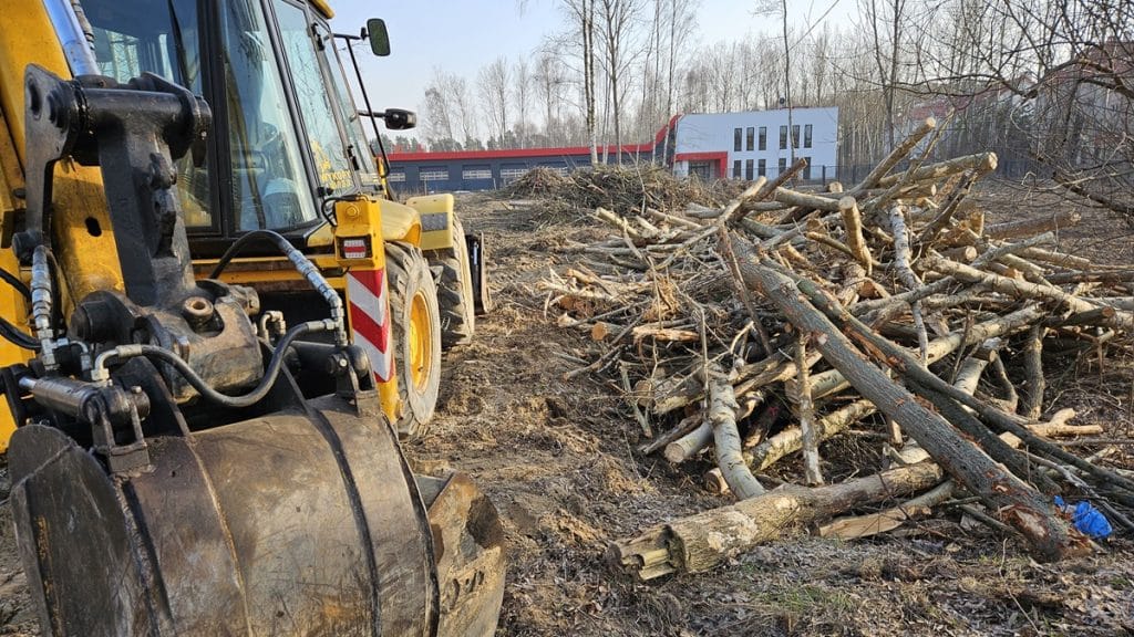 Wycinka drzew na osiedlu Jaroty w Olsztynie przy ulicy Witosa, w tle maszyny i nowoczesny budynek.