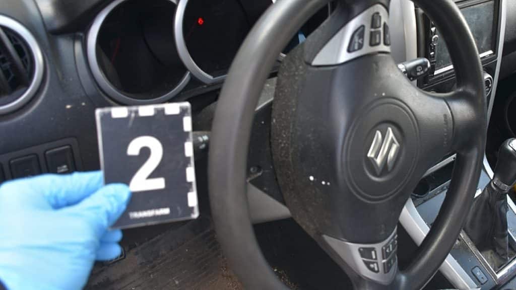 Widok wnętrza samochodu z kierownicą i odciskiem palca na desce rozdzielczej.